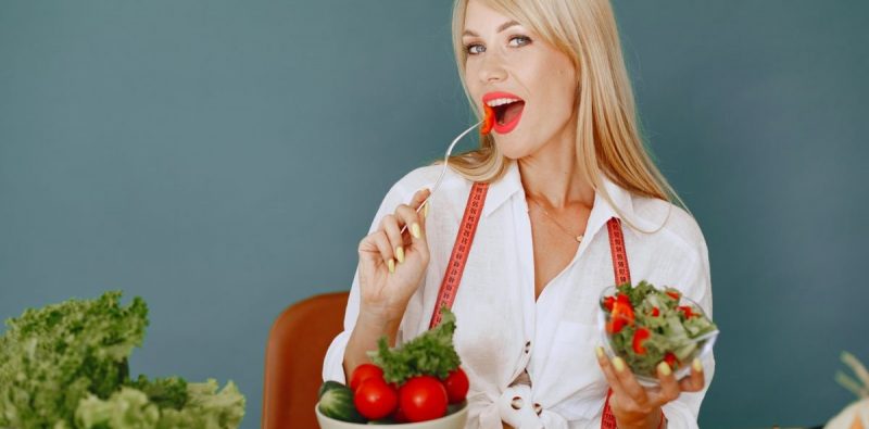 Woman enjoying a fresh salad with tomatoes and greens, promoting healthy eating.